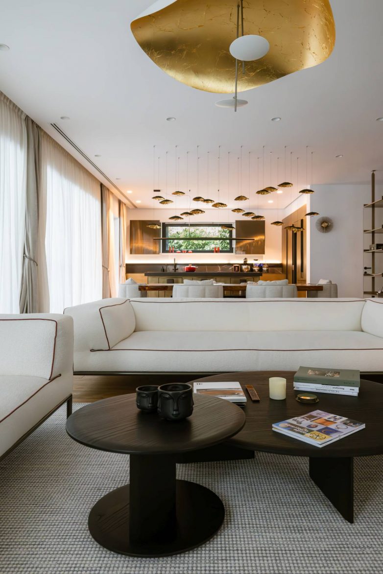 Otvorena dnevna i kuhinjska zona luksuznog stana u Beogradu sa belim sofama, crnim klub-stolićima i zlatnom dizajnerskom rasvetom