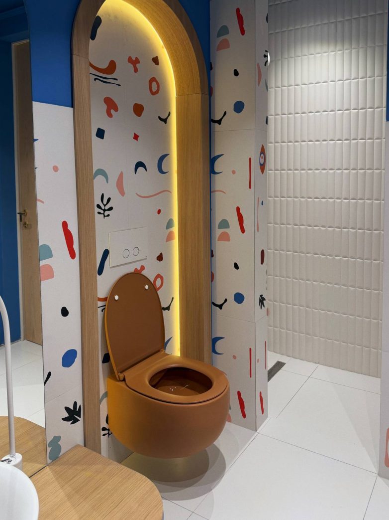 Toalet u dečjem kupatilu smešten u osvetljenoj niši sa ilustrativnim pločicama