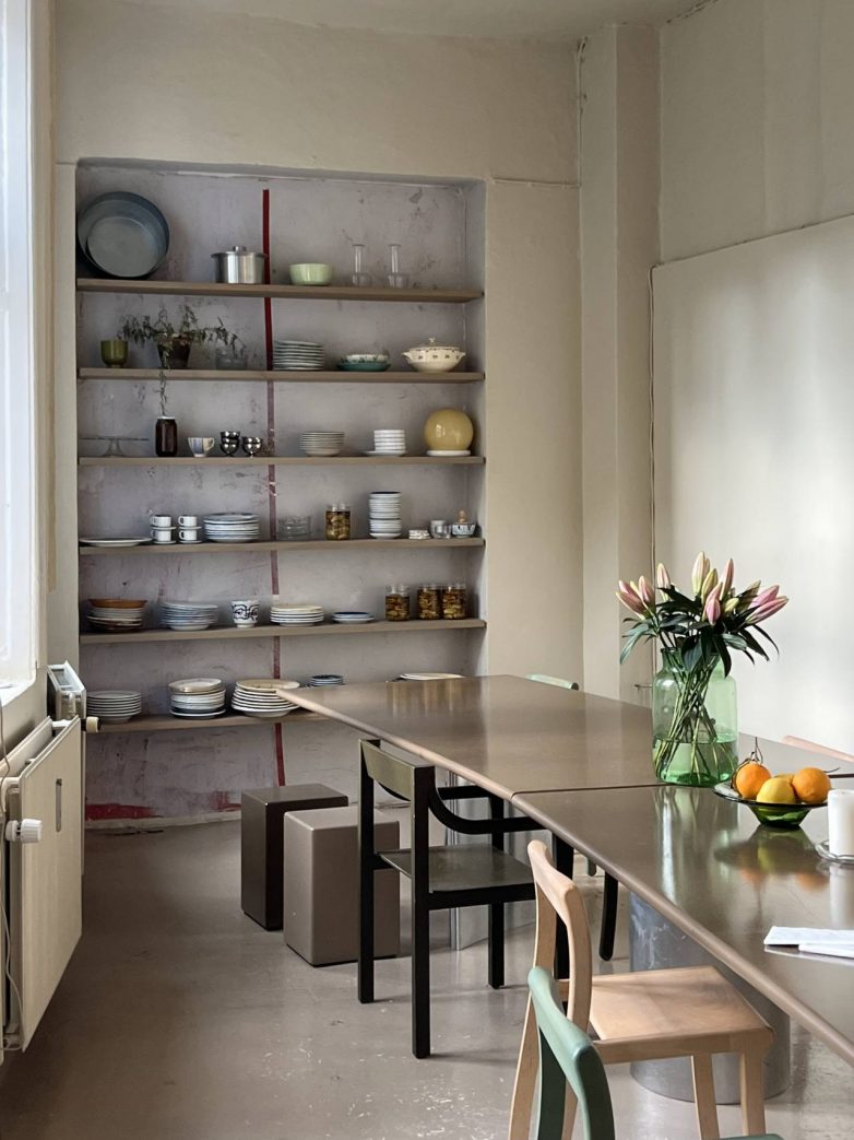 Skandinavska trpezarija sa dugim stolom, otvorenim policama, neutralnim tonovima i jednostavnim keramičkim posuđem