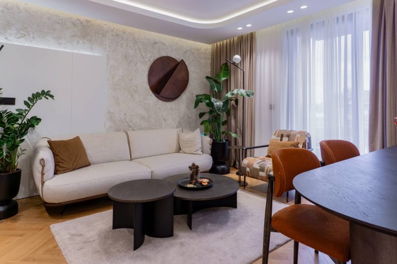 Dnevni boravak porodičnog stana u Beogradu sa teksturiranim zidom, neutralnim nameštajem i toplim tonovima, enterijer Danijele Mišković