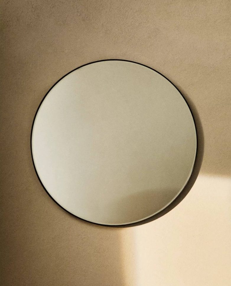 Kružno zidno ogledalo sa tankim crnim metalnim ramom na neutralnoj zidnoj podlozi