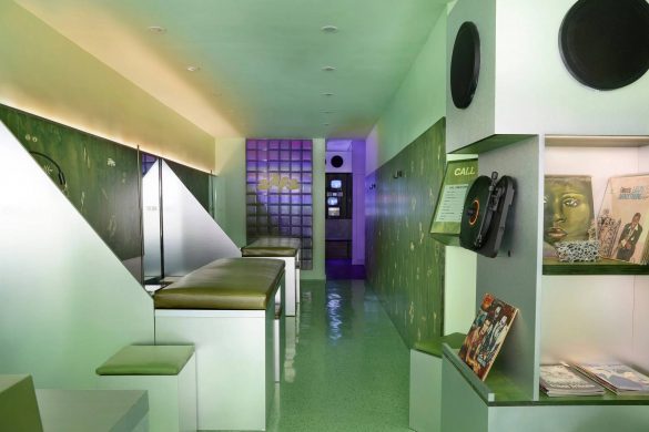 Enterijer salona za mikro-tetovaže Tiny Zaps u Njujorku sa zelenim monohromatskim zidovima, interaktivnim kioscima i klupama za čekanje