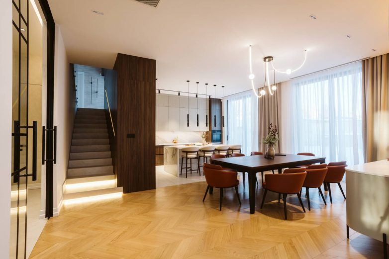 Trpezarija porodične kuće u Srbiji sa velikim drvenim stolom, stepeništem i otvorenom kuhinjom u pozadini