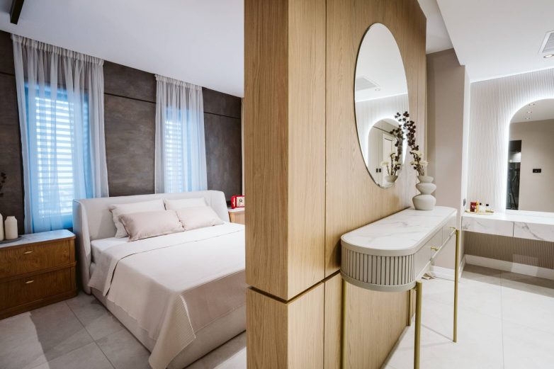 Spavaća soba porodične kuće u Srbiji sa tapaciranim uzglavljem, drvenim ormarima i toaletnim stolom sa ogledalom