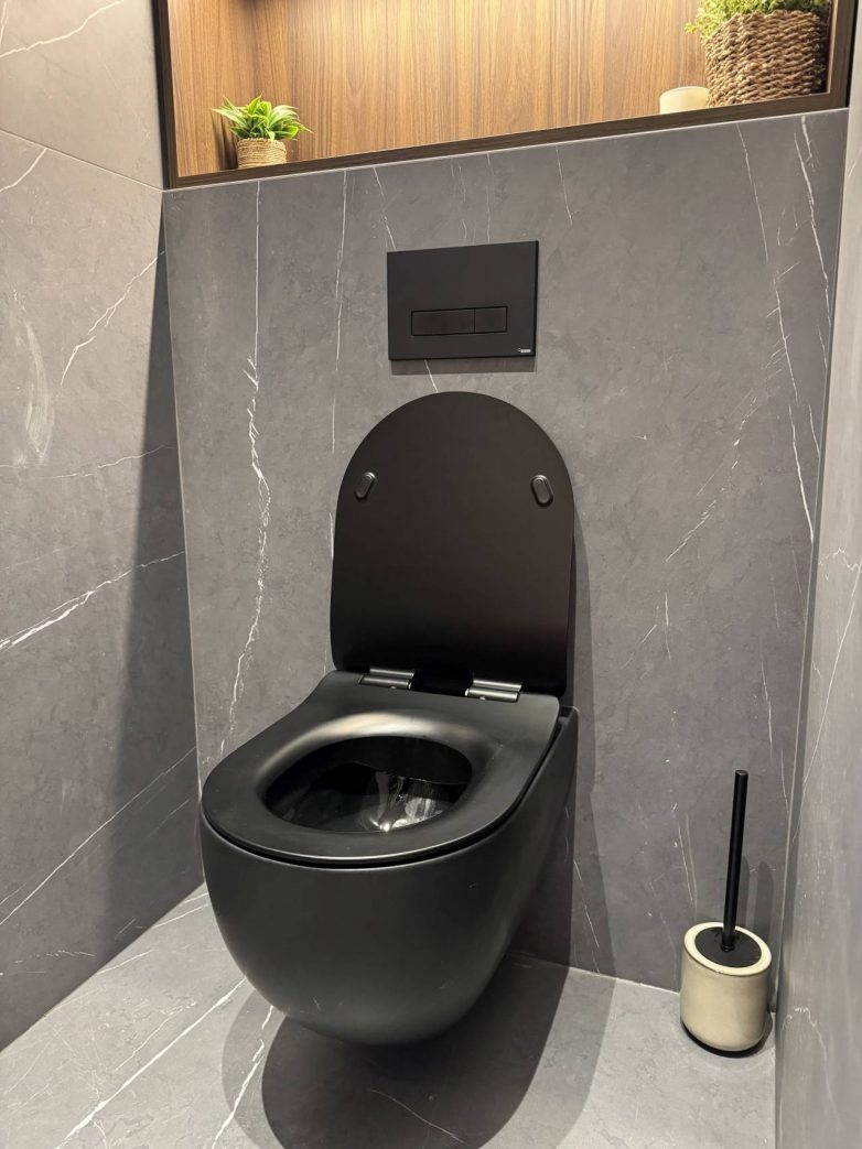 Crna WC šolja u savremenom kupatilu sa sivim keramičkim oblogama i zidnim vodokotlićem