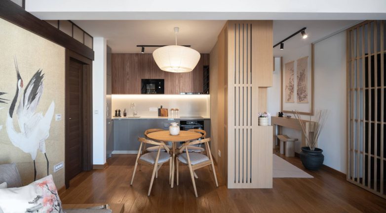 Okrugli trpezarijski sto i kuhinja povezani sa dnevnim boravkom u stanu na Dorćolu sa japanskim detaljima