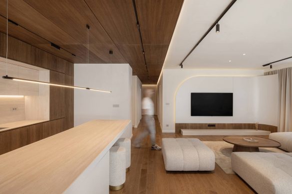 Dnevni boravak i kuhinja u stanu u Nišu sa drvenom plafonskom oblogom, zaobljenim formama i toplim tonovima u enterijeru