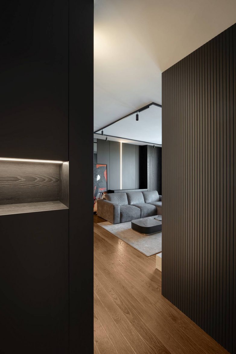Pogled iz komunikacije ka dnevnoj zoni stana od 60 kvadrata u Nišu sa tamnim zidnim oblogama i drvenim podom