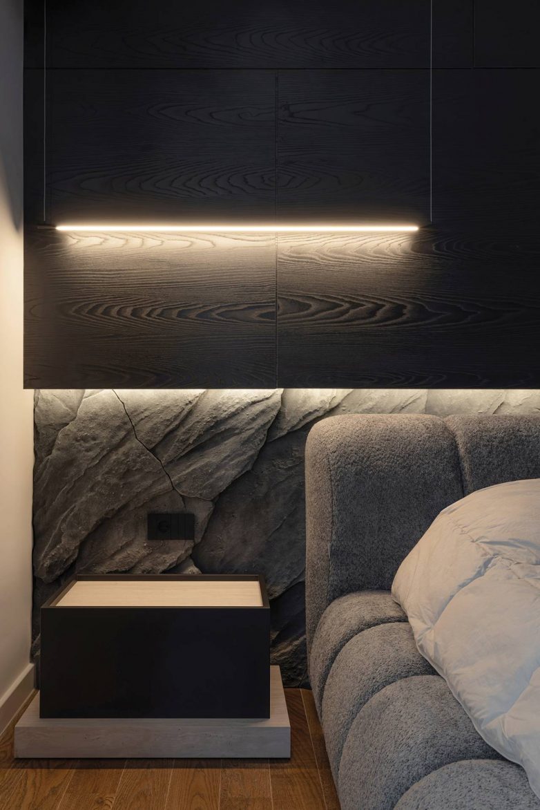 Detalj spavaće sobe u stanu od 60 kvadrata u Nišu sa kamenom oblogom, tapaciranim uzglavljem i ugradnom rasvetom