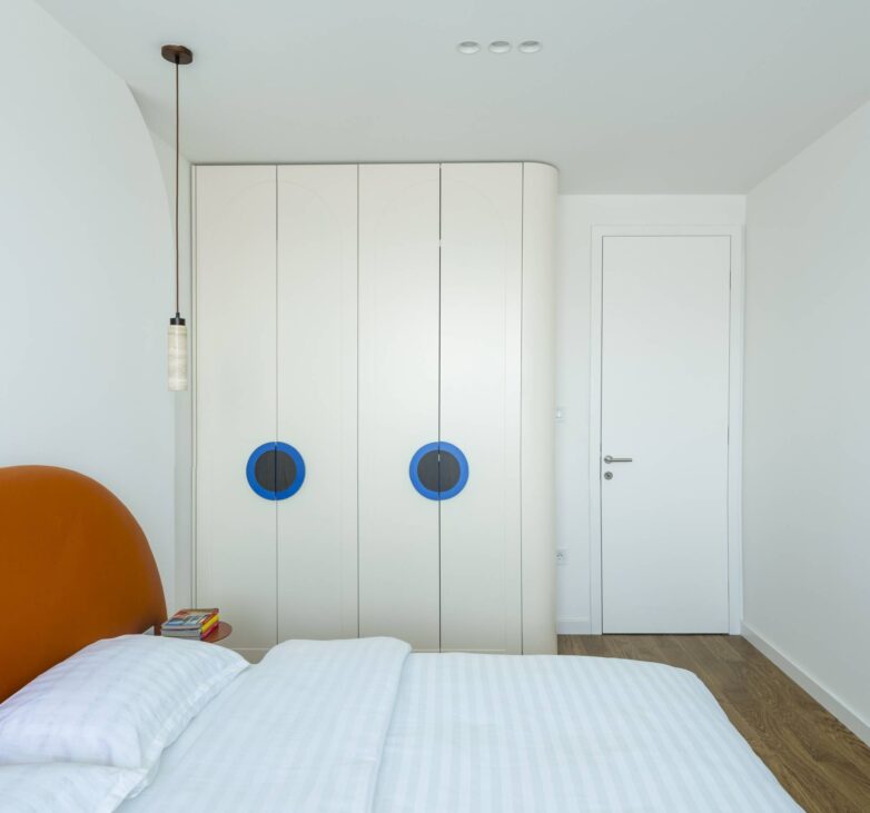 Spavaća soba stana u Banja Luci sa terakota uzglavljem, belim garderoberom i plavim kružnim detaljima na vratima ormara