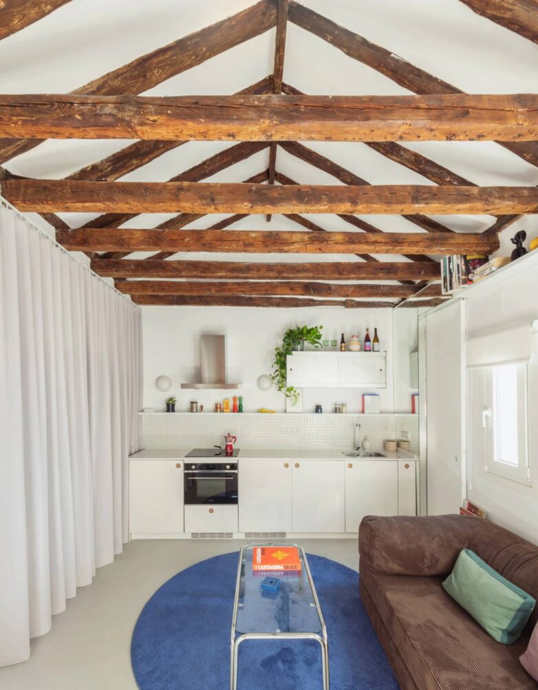 Dnevna soba i kuhinja stana od 30 m2 u Madridu sa otkrivenim drvenim gredama i minimalističkom belom kuhinjom