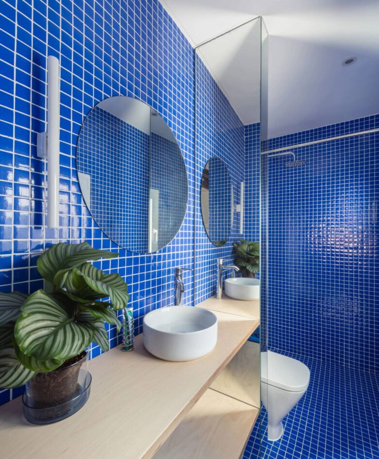 Kupatilo obloženo plavim mozaik pločicama sa okruglim ogledalom i nadgradnim umivaonikom u stanu u Madridu