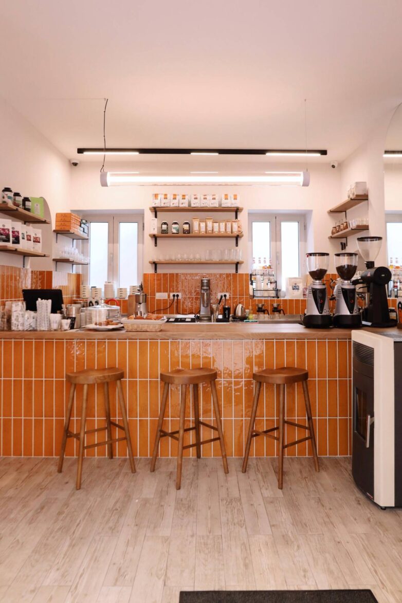 Pult obložen pastelno žutim klinker pločicama sa drvenim barskim stolicama u enterijeru kafeterije u Zemunu