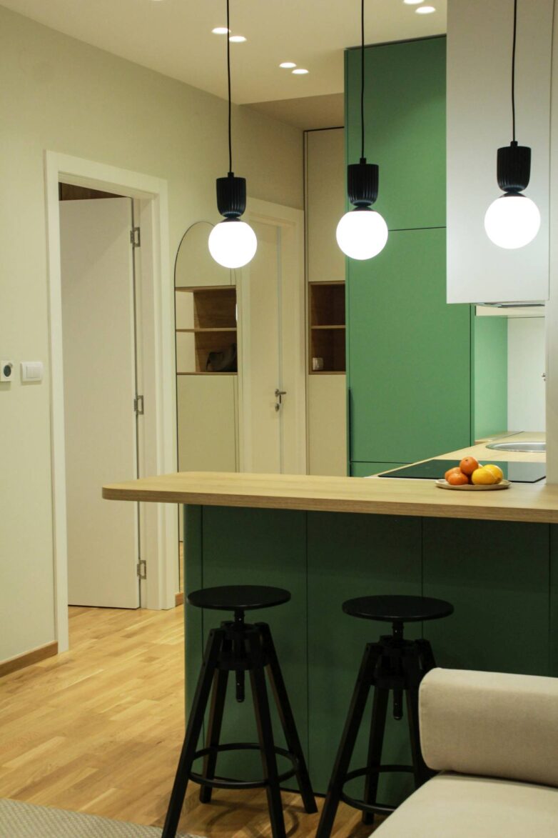 Zelena kuhinja sa drvenim šankom i crnim barskim stolicama u malom stanu u Novom Sadu