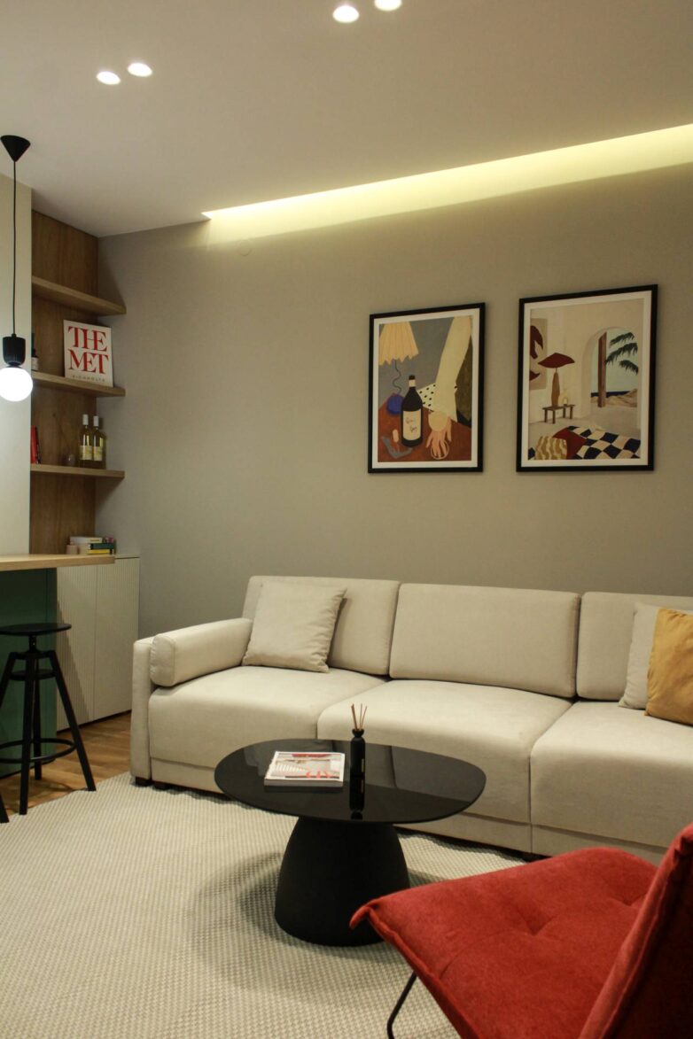 Dnevni boravak stana od 38 m2 u Novom Sadu sa bež sofom, crnim klub stolom i umetničkim slikama