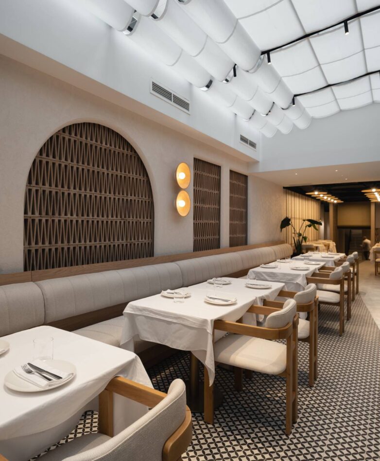 Enterijer restorana VID u Beogradu sa dugom tapaciranom klupom, drvenim stolicama, geometrijskim podom i svetlom staklenom plafonskom konstrukcijom