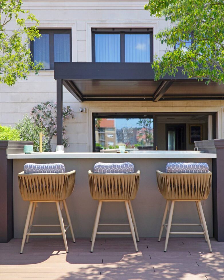 Otvorena kuhinja na krovnoj terasi u Valjevu sa kamenim pultom, tri barske stolice i bioklimatskom pergolom