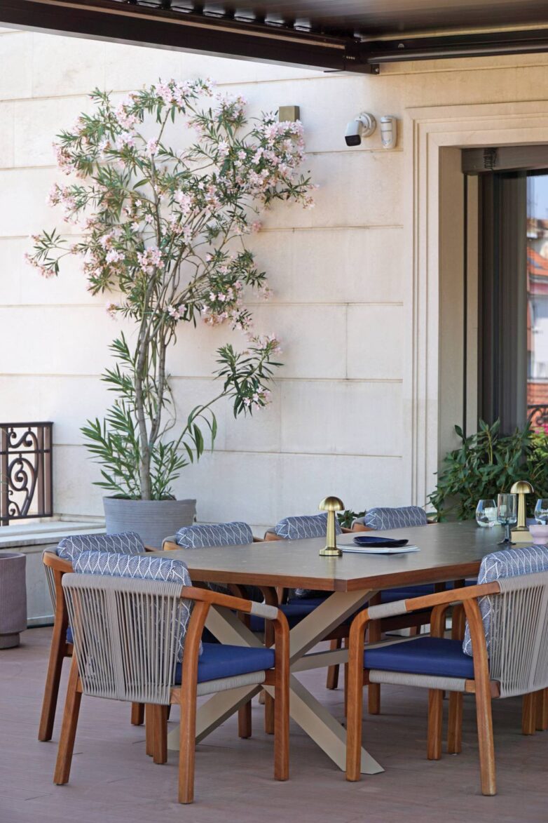 Trpezarijski sto sa drvenim stolicama na krovnoj terasi u Valjevu, ispod bioklimatske pergole i uz dekorativno zelenilo