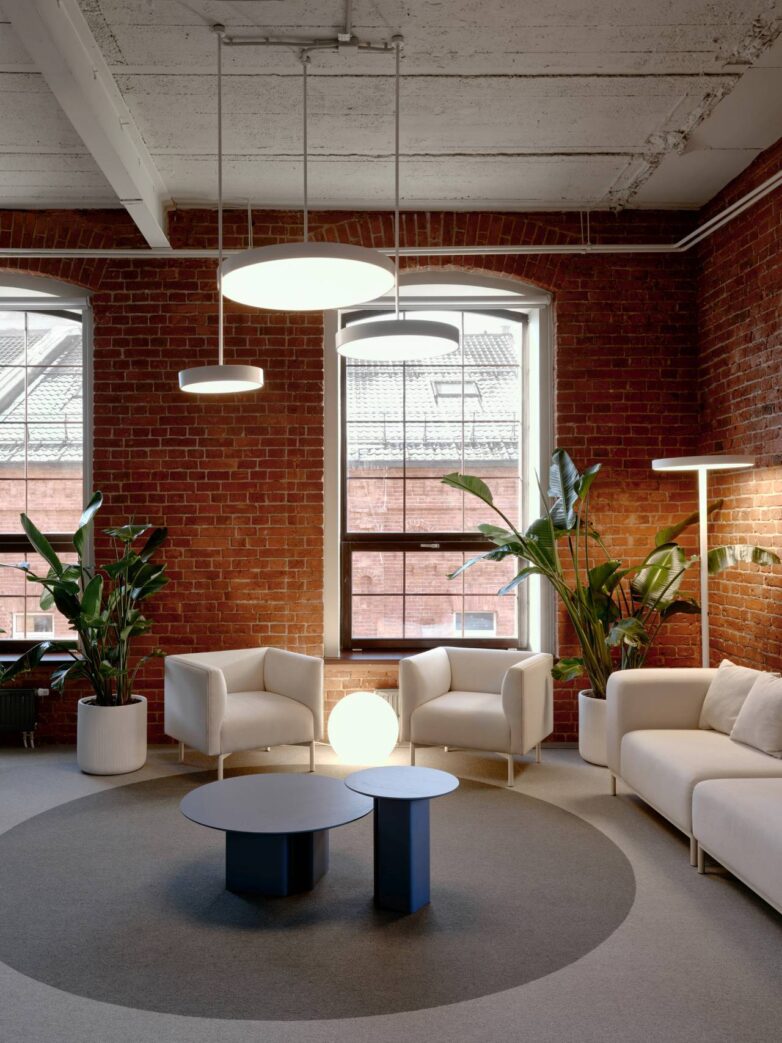 "Lounge" zona kancelarije Yandex u Moskvi sa belim foteljama, crvenim zidovima od opeke i velikim prozorima u industrijskoj zgradi