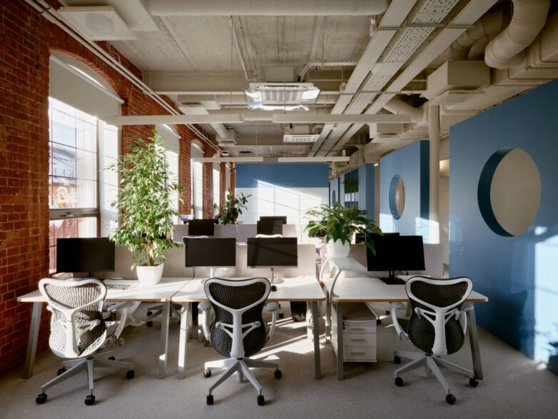 "Open-space" radna zona kancelarije Yandex u Moskvi sa ergonomskim stolicama, belim radnim stolovima, zidovima od opeke i plavim pregradama sa kružnim otvorima