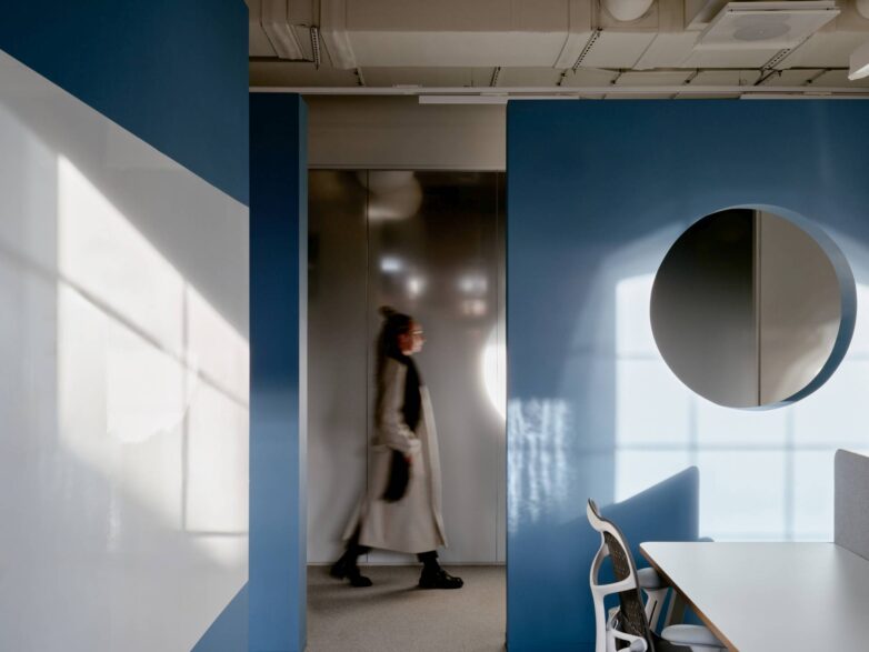 Plava pregrada sa kružnim otvorom u kancelariji Yandex u Moskvi, sa radnim stolom i ergonomskom stolicom u "open-space" zoni