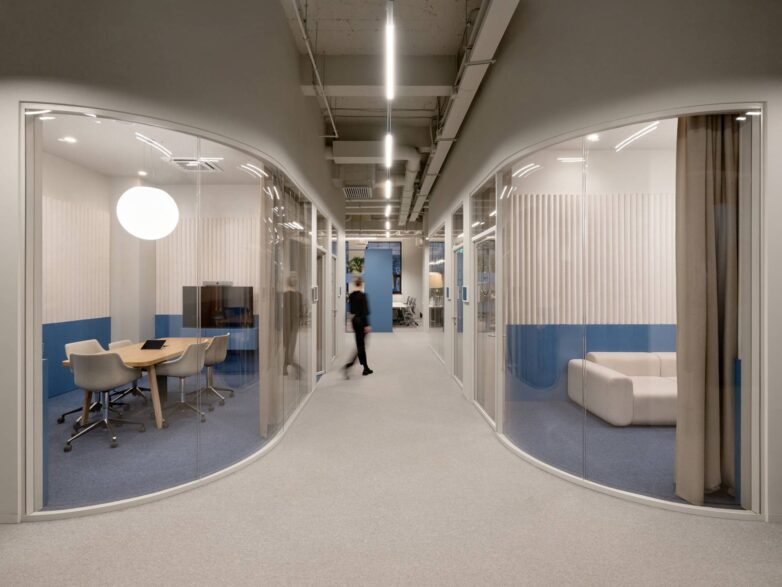 Hodnik kancelarije Yandex u Moskvi sa zakrivljenim staklenim salama za sastanke, plavim panelima i sivim tepihom