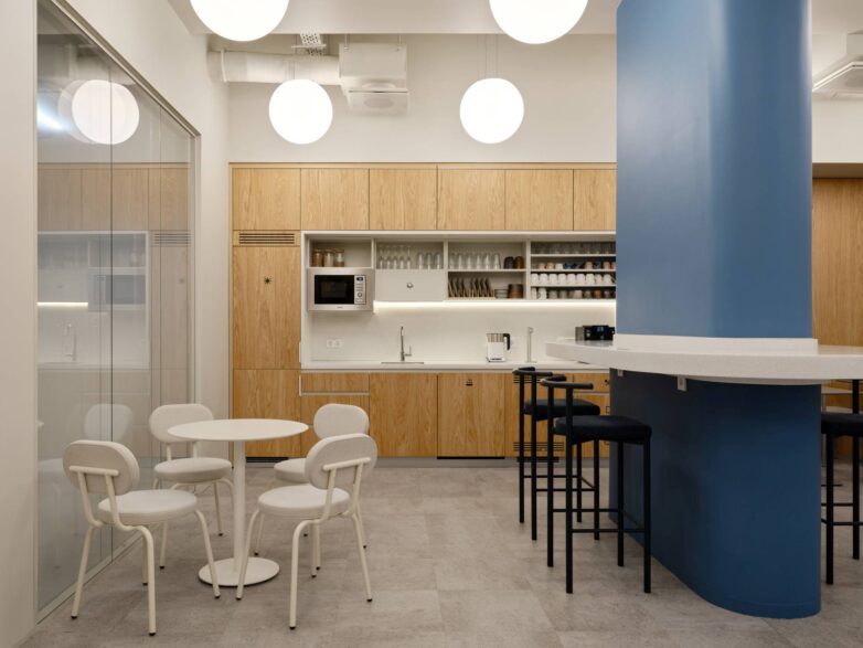 Kafeterija kancelarije Yandex u Moskvi sa drvenim kuhinjskim elementima, plavim stubom sa šankom i belim okruglim stolom