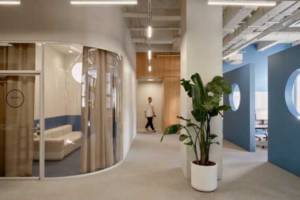 Hodnik kancelarije Yandex u Moskvi sa zakrivljenom staklenom salom za sastanke, plavim pregradama sa kružnim otvorima i velikom biljkom u saksiji