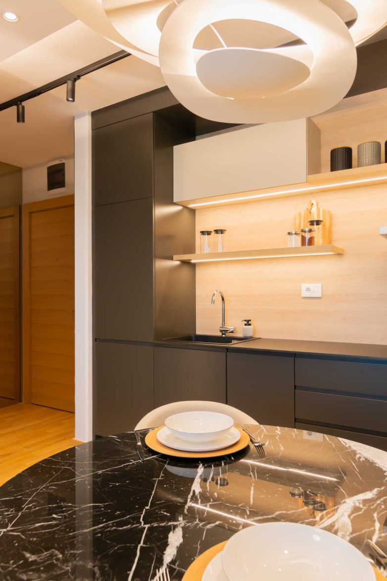 Crna mat kuhinja sa antifinger frontovima, drvenom oblogom zida i otvorenim policama sa LED osvetljenjem