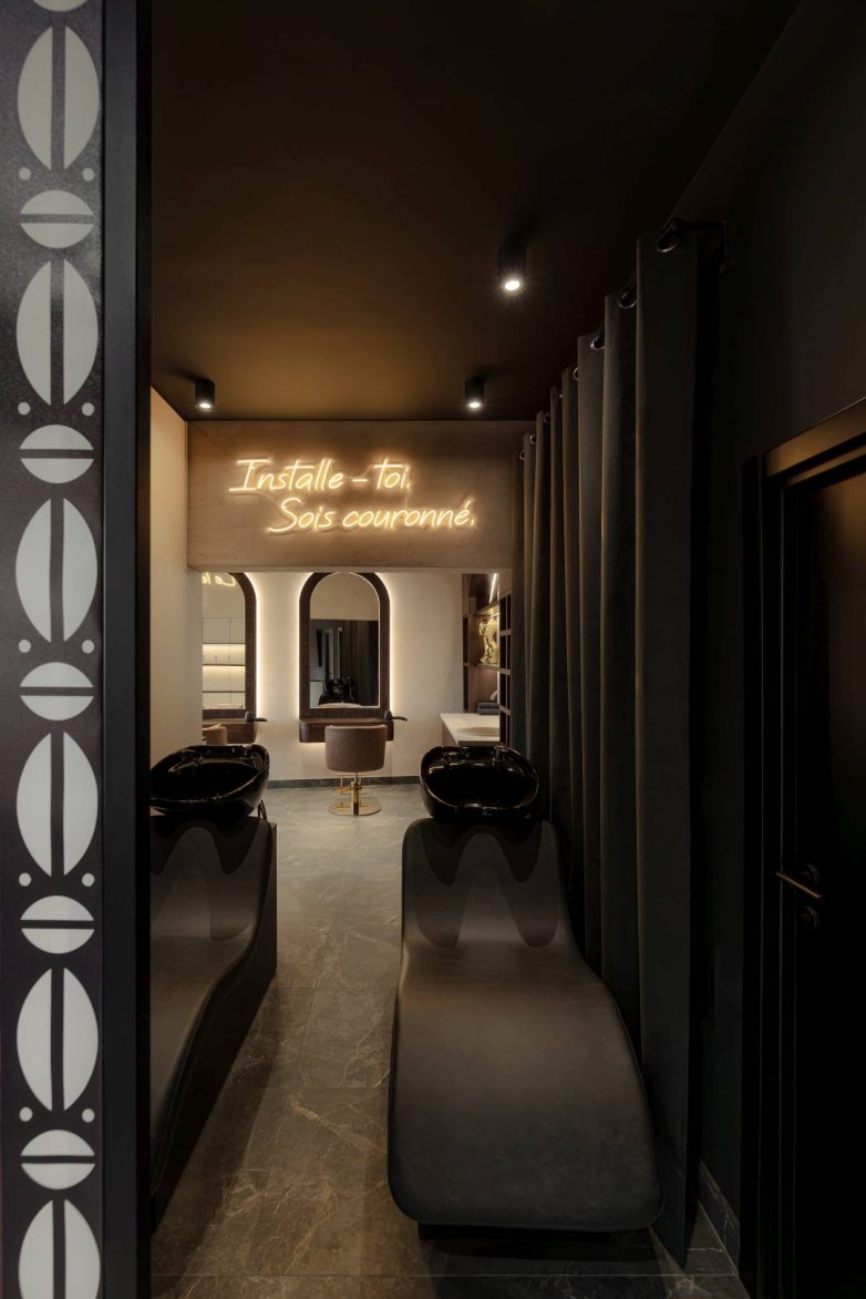 Zona za pranje kose u salonu L'Atelier 35 sa crnim stolicama i neonskim natpisom na zidu