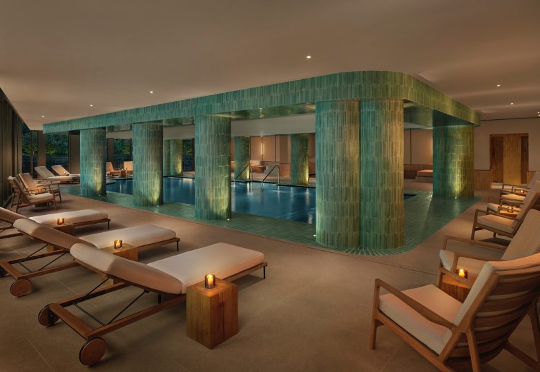 Luksuzni spa prostor sa bazenom, zelenim keramičkim stubovima i ležaljkama u toplom ambijentu