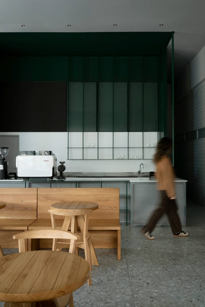 Šank u Kafeteriji u Čačku sa zelenim zidnim panelima, rebrastim staklom i drvenim klupama u prvom planu, projekat KIDZ Studio