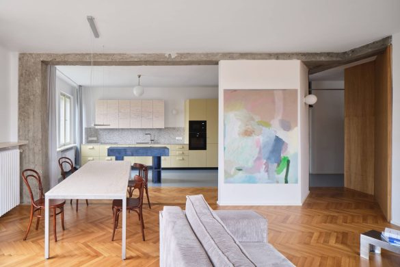 Otvoren dnevni prostor sa trpezarijom i kuhinjom u pastelnim tonovima, tamno plavo ostrvo i hrastov parket u stanu u Pragu