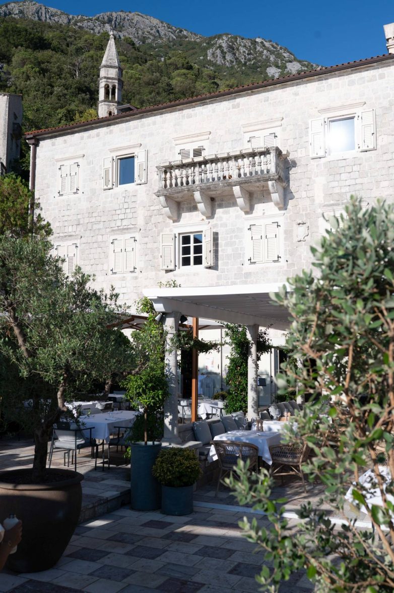 Kamena palata u Perastu sa baštom restorana u prizemlju i planinama u pozadini