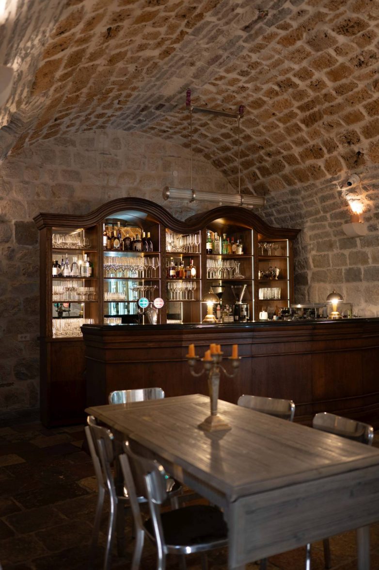 Drveni bar i vinska vitrina u enterijeru restorana Eho u Perastu sa kamenim svodovima