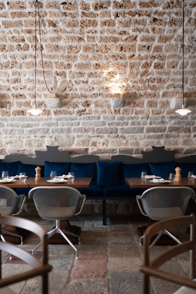 Kameni zid i tapacirana klupa sa plavim jastucima u enterijeru restorana Eho u Perastu
