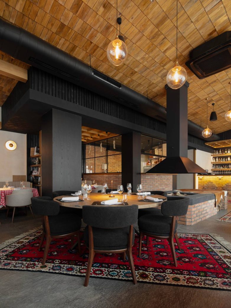 Veliki okrugli sto za goste u restoranu Stena u Beogradu pored otvorenog ložišta, sa drvenim plafonom i zidovima od opeke