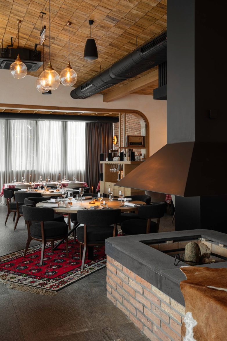 Okrugli sto za goste u restoranu Stena u Beogradu sa crvenim ćilimom i ognjištem od opeke