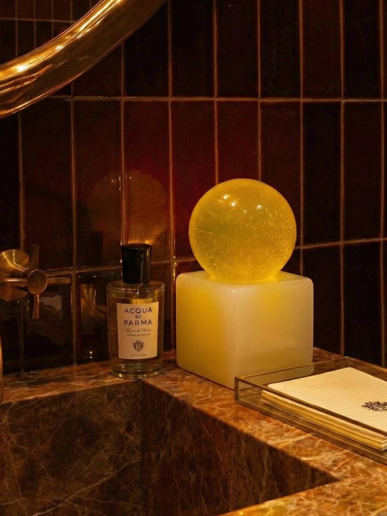 Žuta prozirna sfera sapuna na kockastoj bazi pored lavaboa sa tamnim pločicama