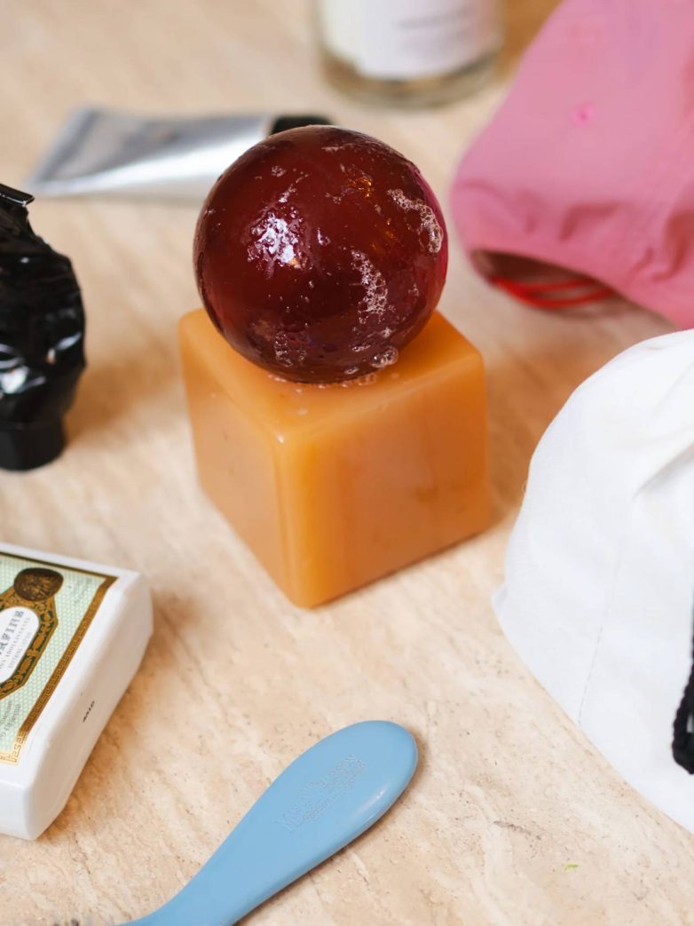 Tamna sfera sapuna postavljena na narandžastu kockastu bazu na kupatilskom pultu