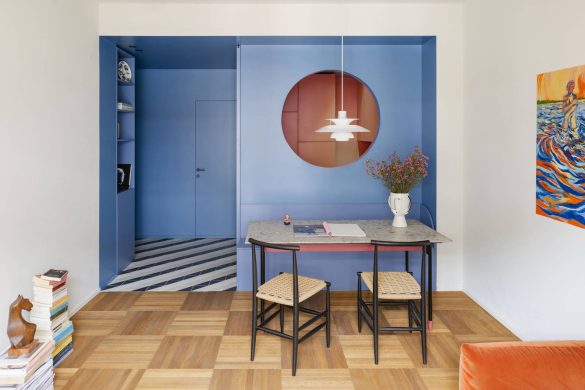 Trpezarijski deo stana u Milanu sa plavom nišom, okruglim otvorom prema kuhinji i parketom u kvadratnom rasteru