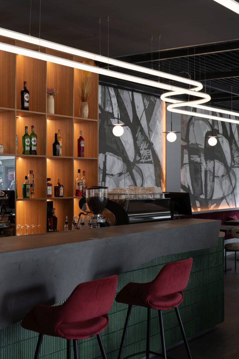 Šank u baru u Beogradu sa policama za piće, zelenim pločicama i visećom svetlosnom instalacijom