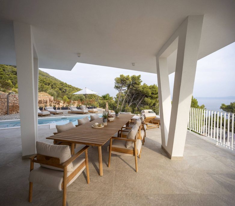 Natkrivena terasa vile Vinea Privata na Hvaru sa velikim drvenim stolom, bazenom i pogledom na more