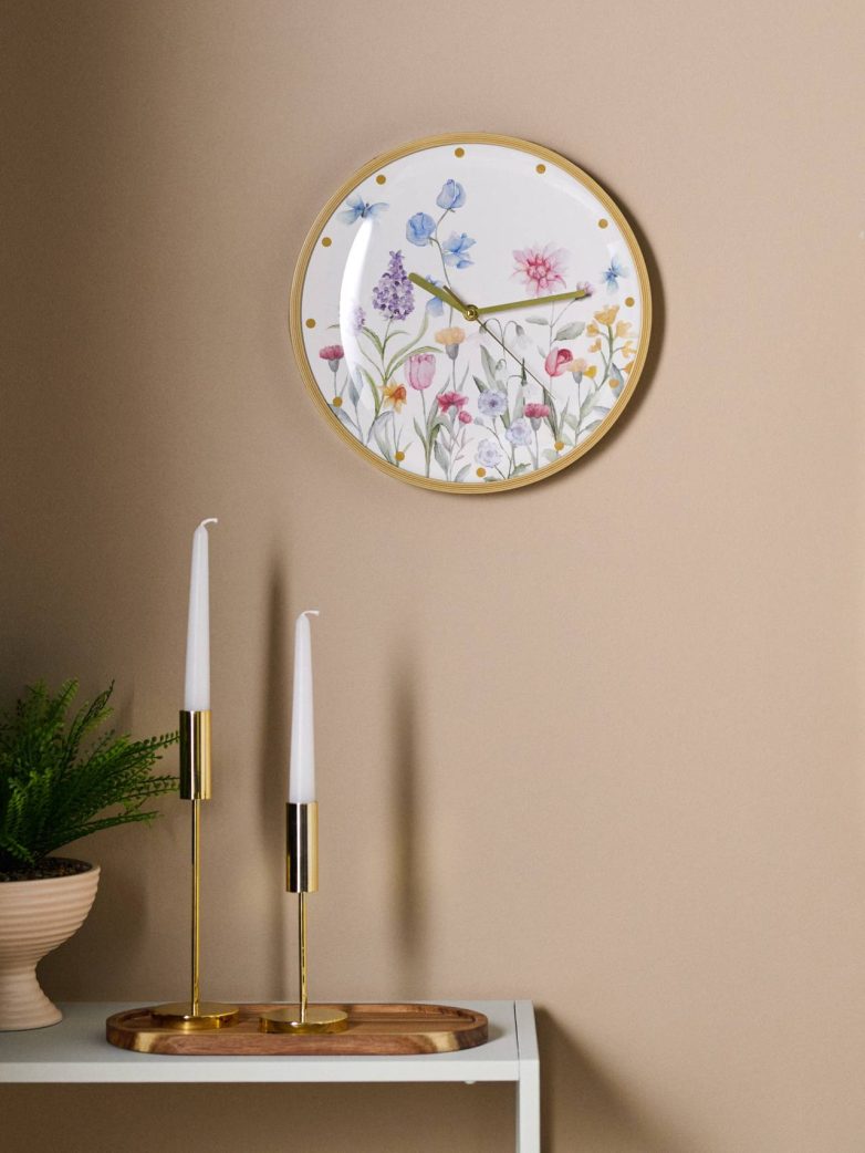 Zidni sat sa cvetnim motivom i zlatnim ramom na bež zidu