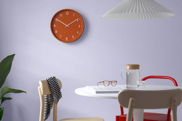 Narandžasti zidni sat na zidu u svetlom enterijeru sa trpezarijskim stolom