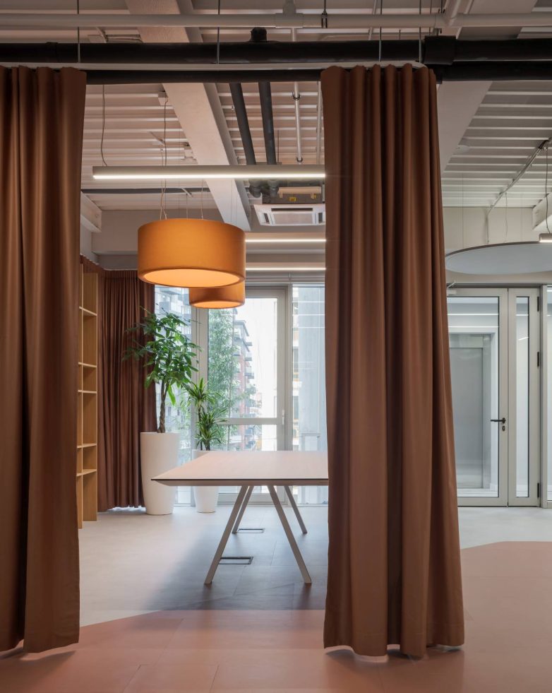 Prostor sa zavesama koje razdvajaju zone, stolom za sastanke i visećim lampama u Aneksu Ložionice u Beogradu