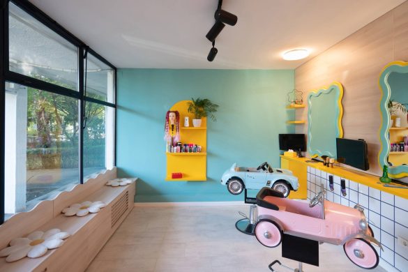 Enterijer dečjeg frizerskog salona sa šarenim zidovima, klupom uz prozor i frizerskim stolicama u obliku automobila