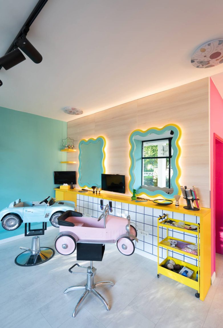 Frizerski deo sa ogledalima nepravilnog oblika, žutim elementima i stolicama u obliku automobila