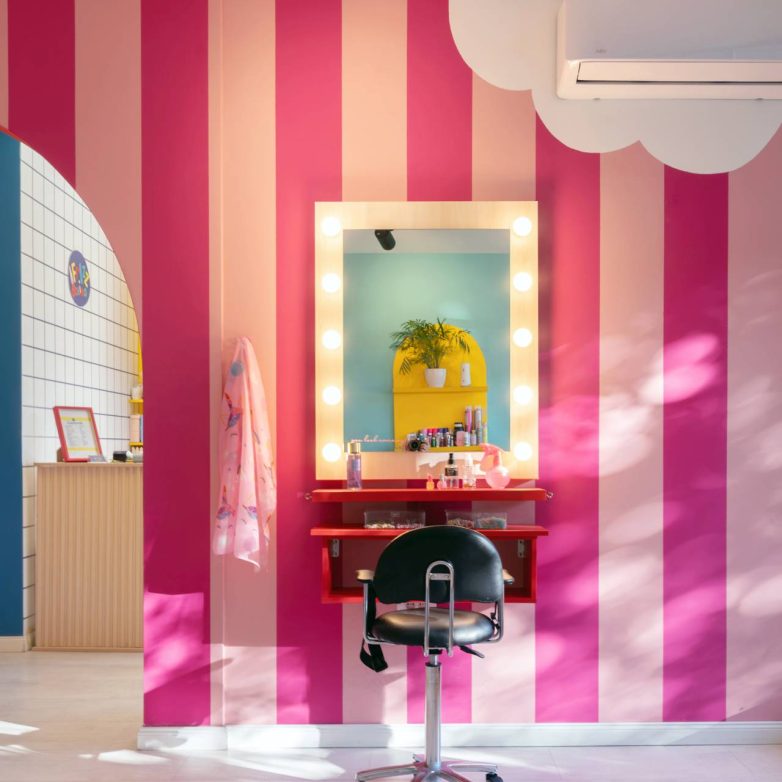 Frizersko mesto sa ogledalom i svetlima na roze prugastom zidu u dečjem salonu