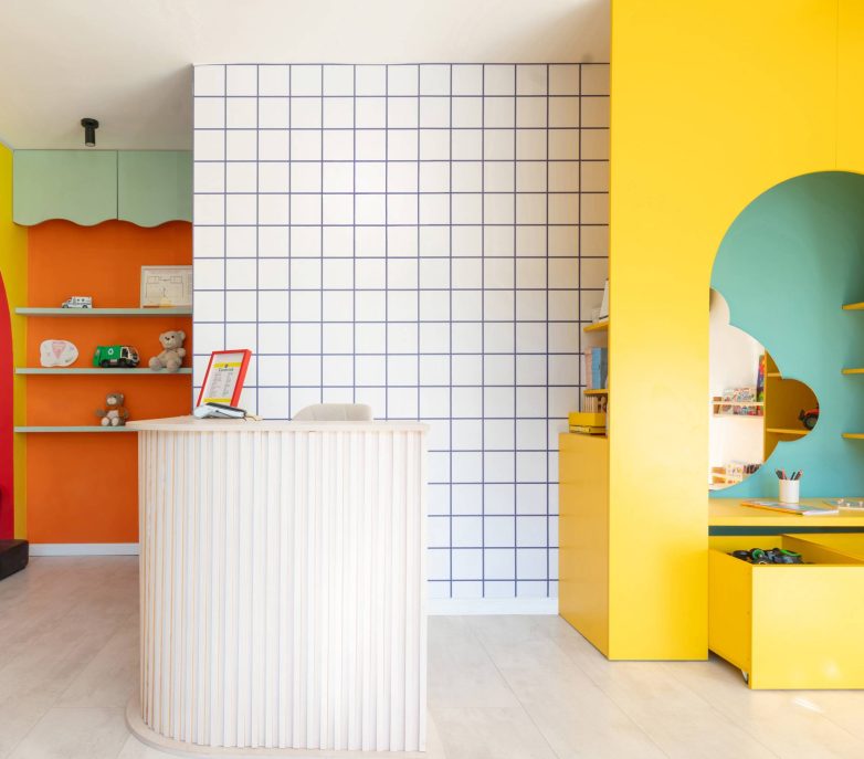 Recepcija dečjeg salona sa belim pultom, zidom sa kvadratnim pločicama i šarenim zonama za igru